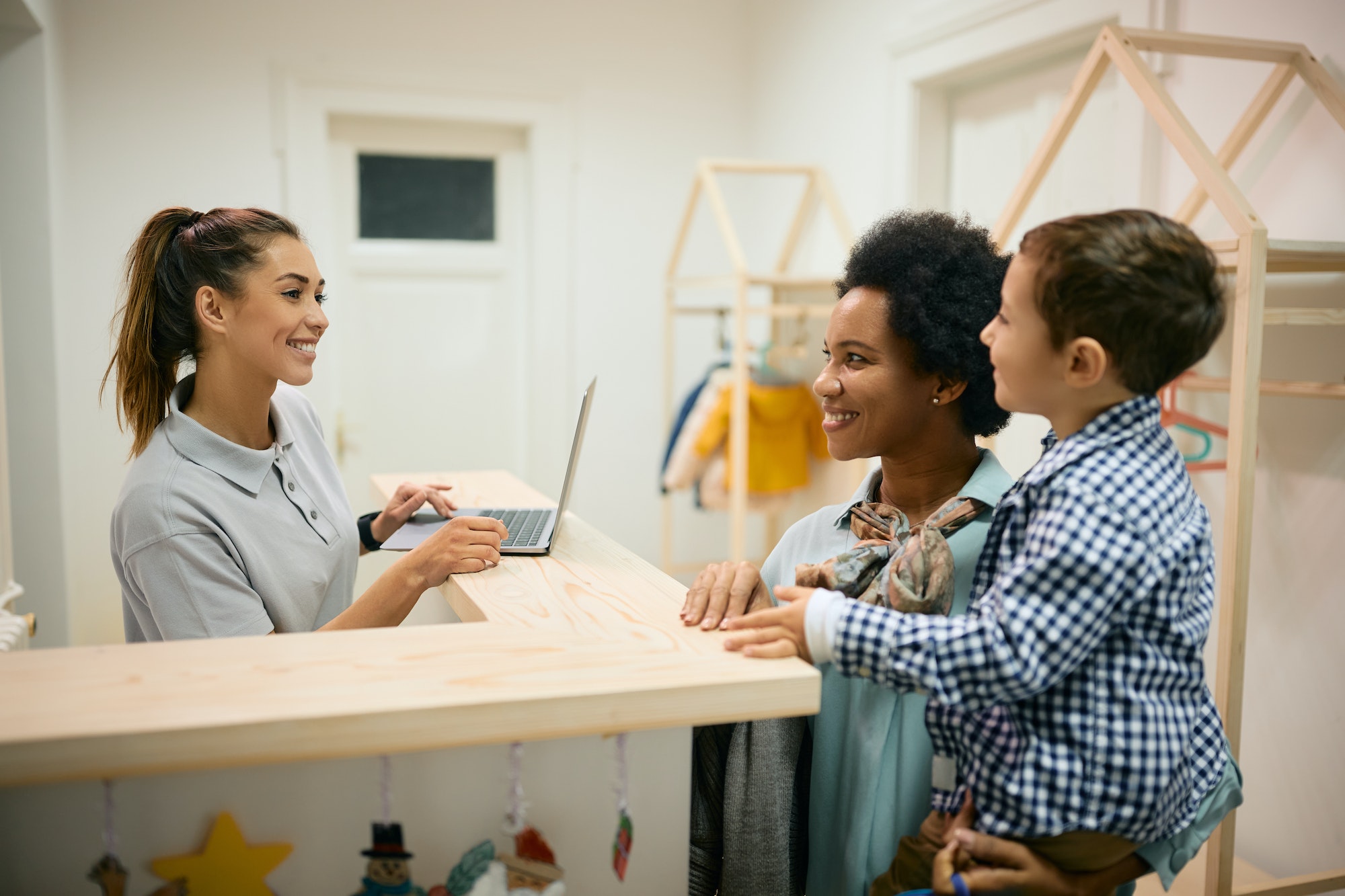 Happy black mother and her son talking to a teacher at reception desk at daycare.